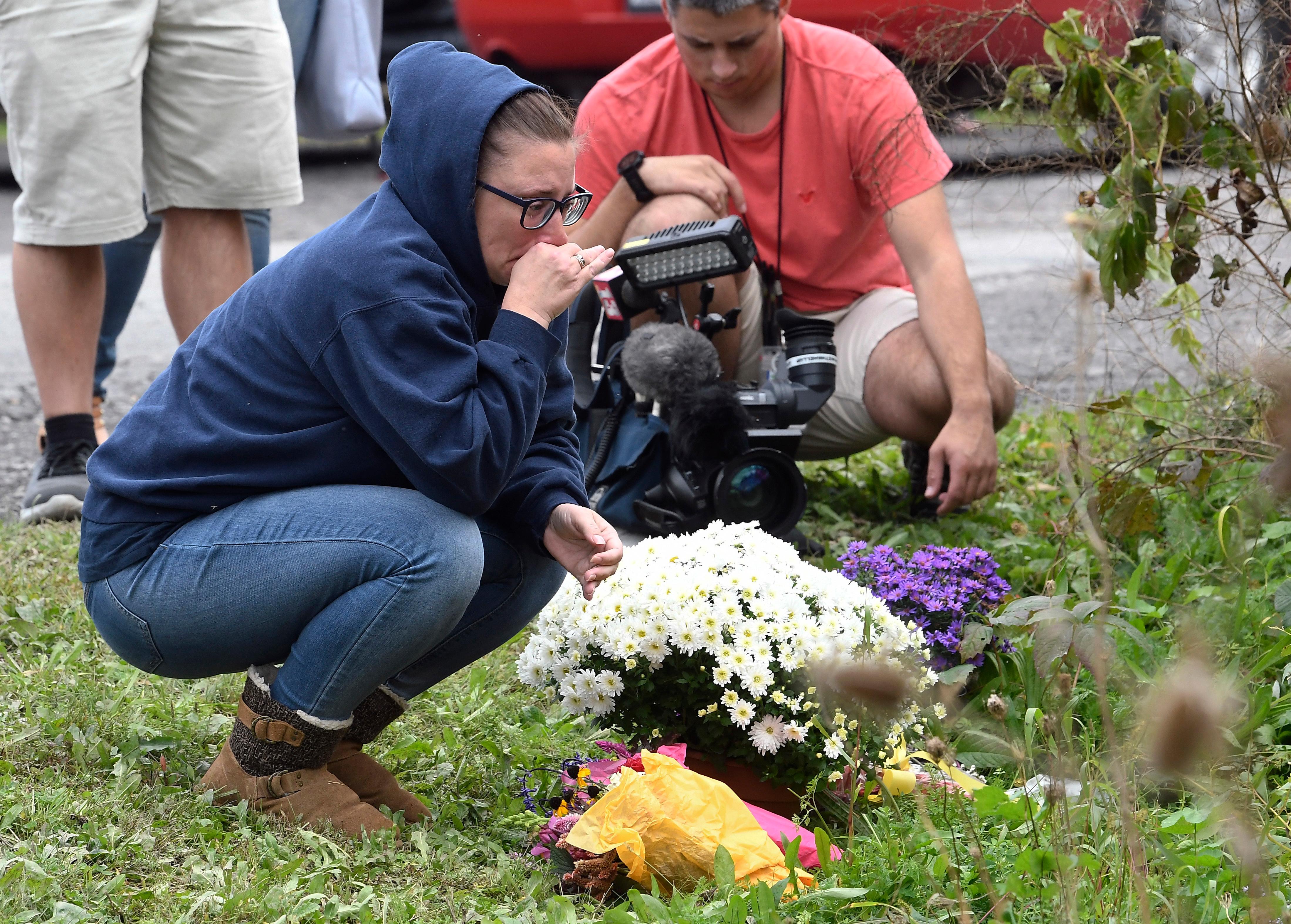 a woman kneels after placing flowers, sunday, oct.